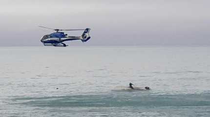 A helicopter flies overs an upturned boat in New Zealand