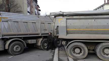 man passes by a barricade made of trucks loaded with stones