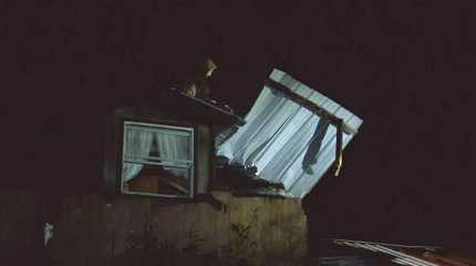 worker moves debris on top of damaged house