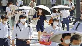 People, some of them holding parasols, cross an intersection amid heat