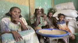 Tesfay center sits with his wife and grandchildren who have been displaced for 18 months